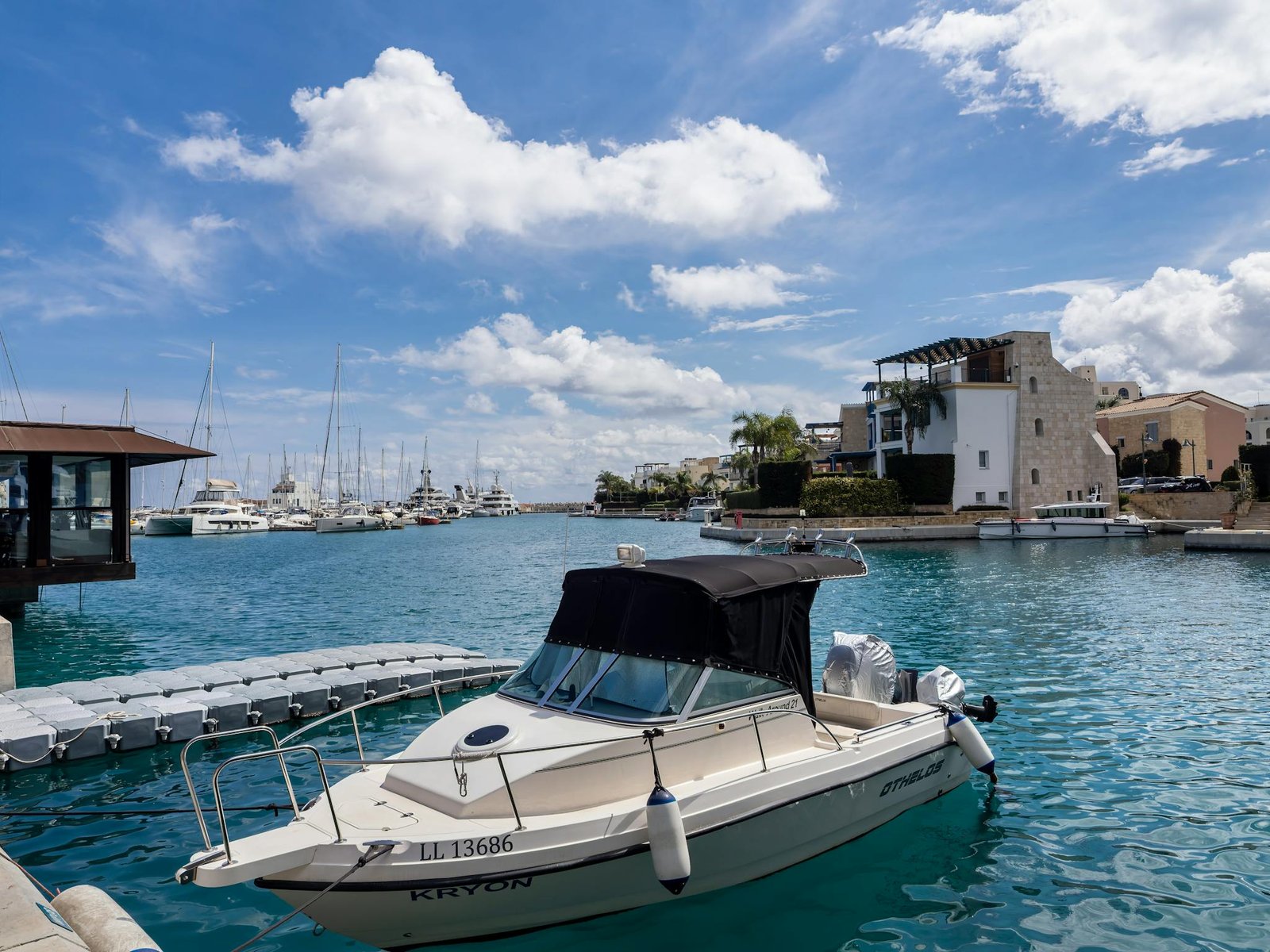 A luxury boat docked at a vibrant Mediterranean marina under clear skies, perfect for summer travel.